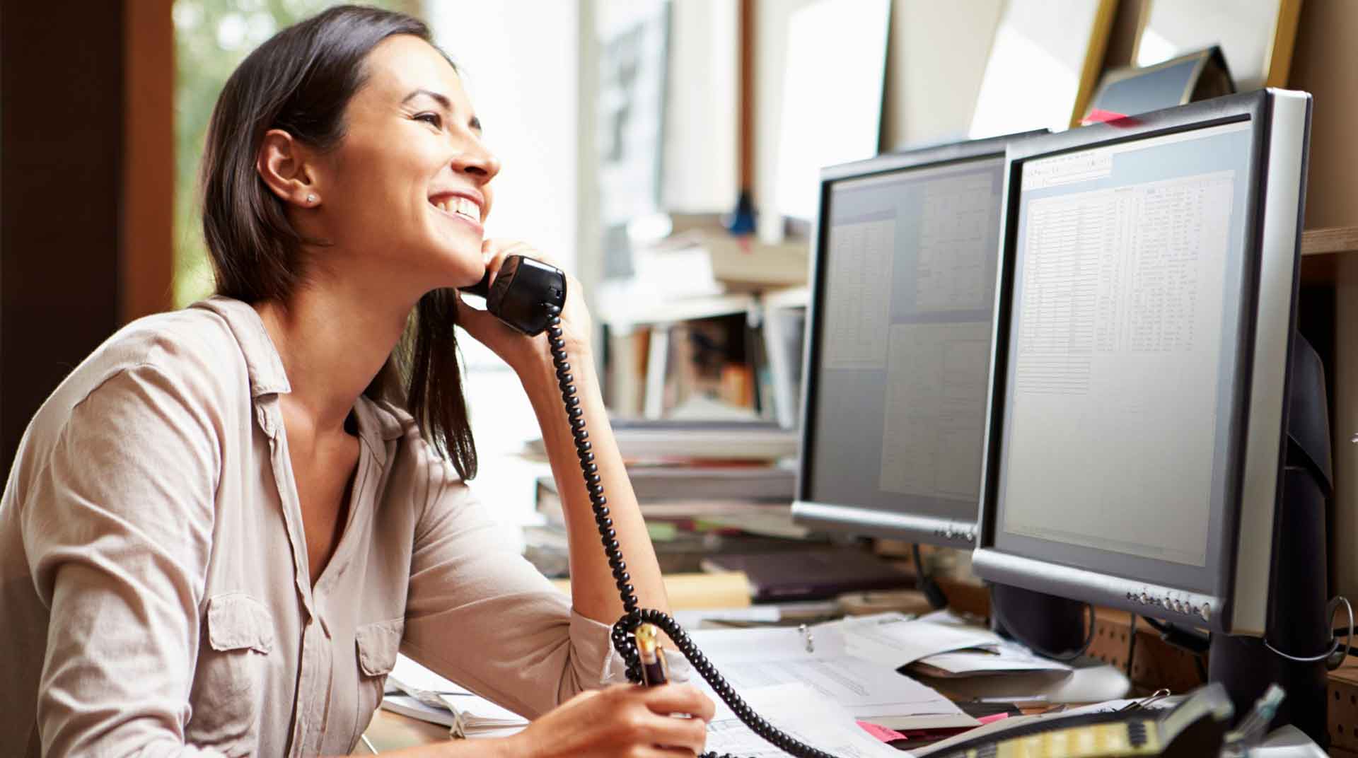 Woman smiling while on the phone, sitting at her desk with her computer