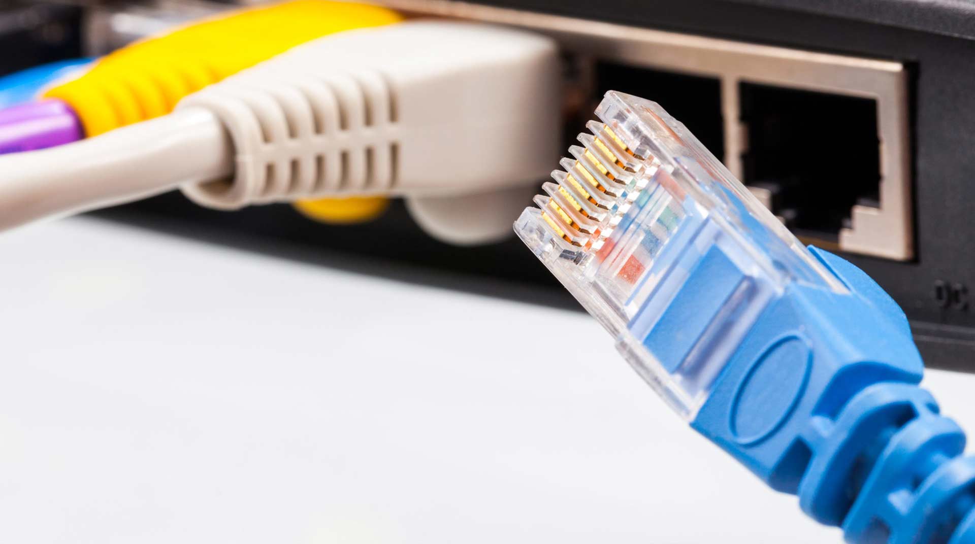 Close-up of a blue Ethernet cable with a visible connector, poised near an internet router with multiple colored cables plugged into its ports, ready to ensure seamless internet connectivity alongside the Wi-Fi network.