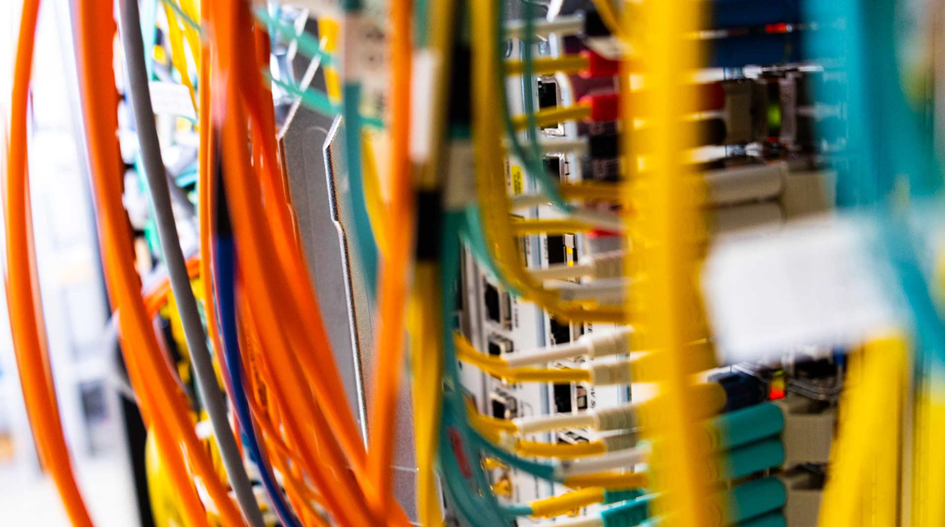 Close-up of a network server with numerous colorful cables, including orange, green, and yellow wires, plugged into it. The image captures the complexity and organization of a private line within a data center or IT infrastructure setup.