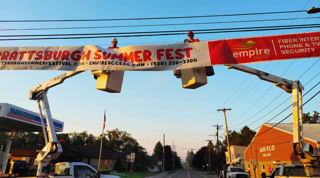 Empire Access employees using equipment to install a community banner in Prattsburgh, NY demonstrating who Empire Fiber Internet is.