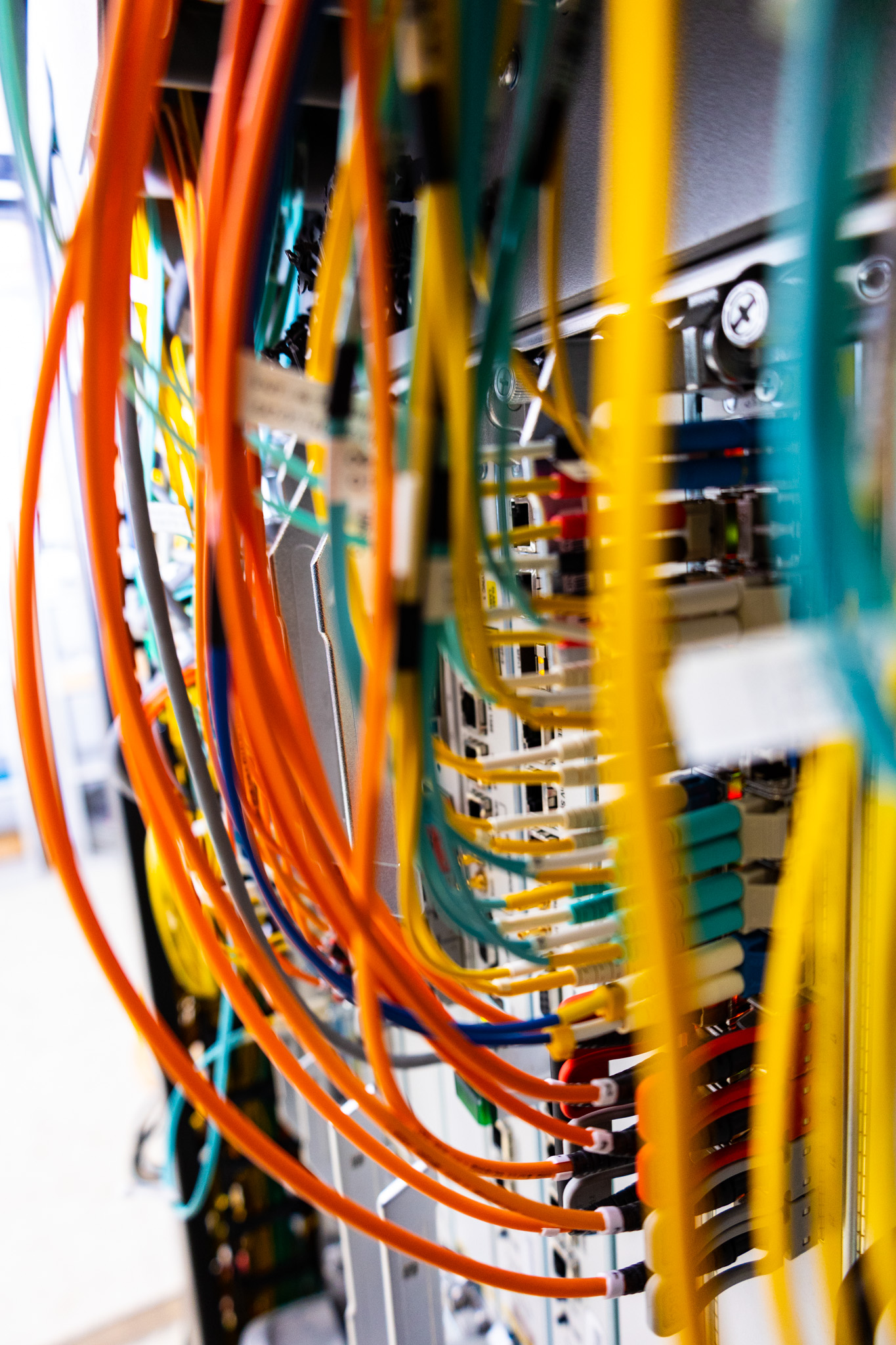 Close-up of a network server with numerous colorful cables, including orange, green, and yellow wires, plugged into it. The image captures the complexity and organization of a private line within a data center or IT infrastructure setup.