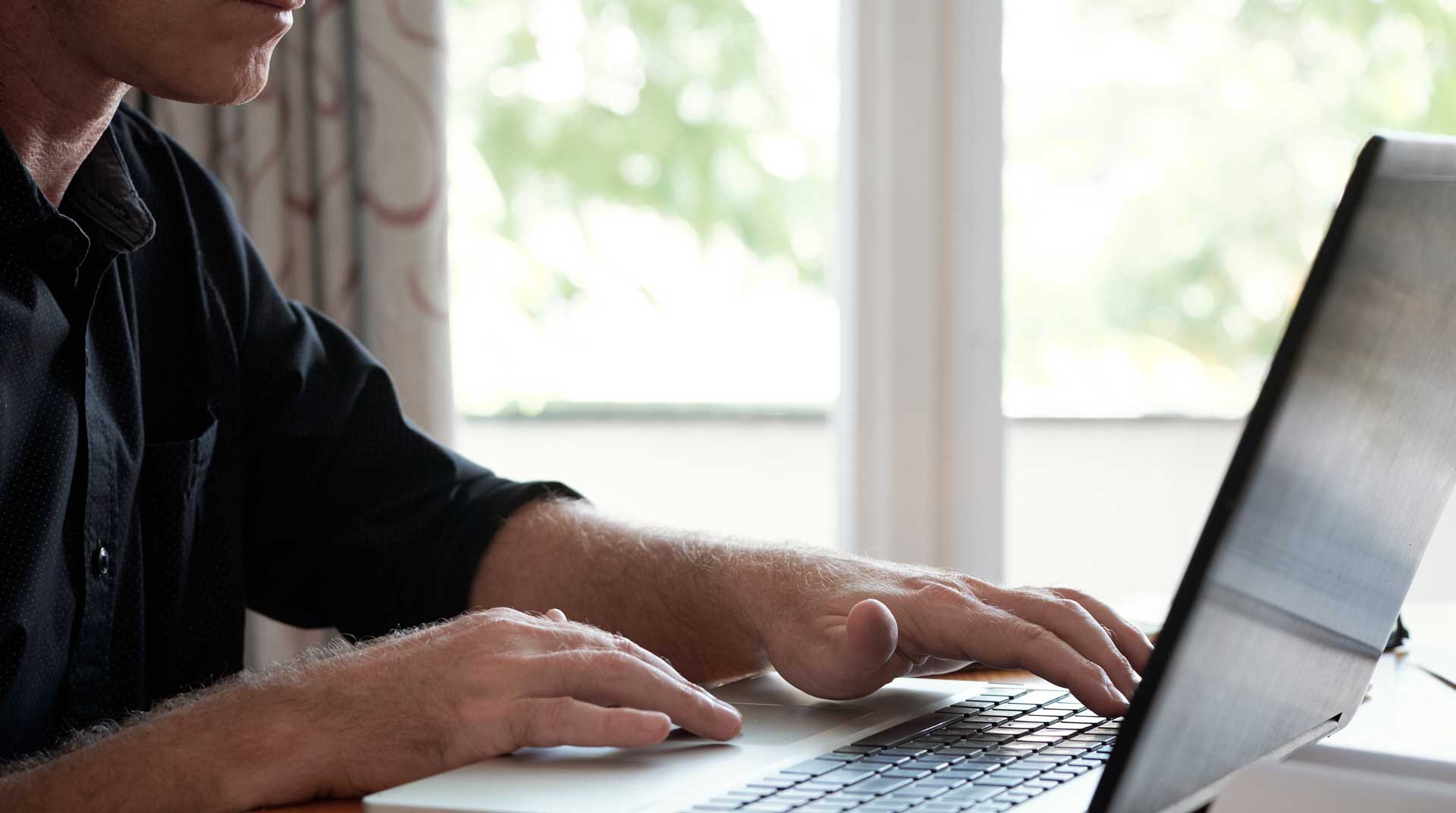closeup of a man sitting at a table using his laptop