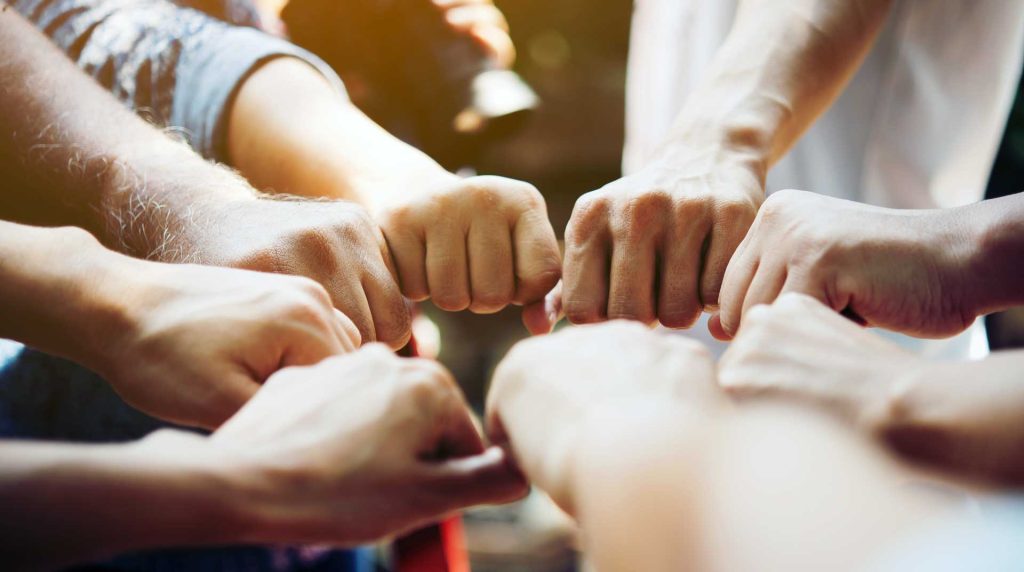 group of people in a circle with their fists put together demonstrating teamwork