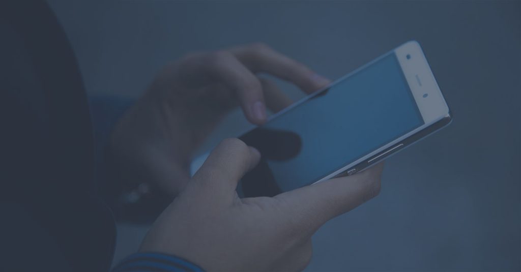 A person holding a smartphone with both hands, engaging with an online directory on the screen. The background is blurred, emphasizing the device and hands. The image has a cool, blue tint.