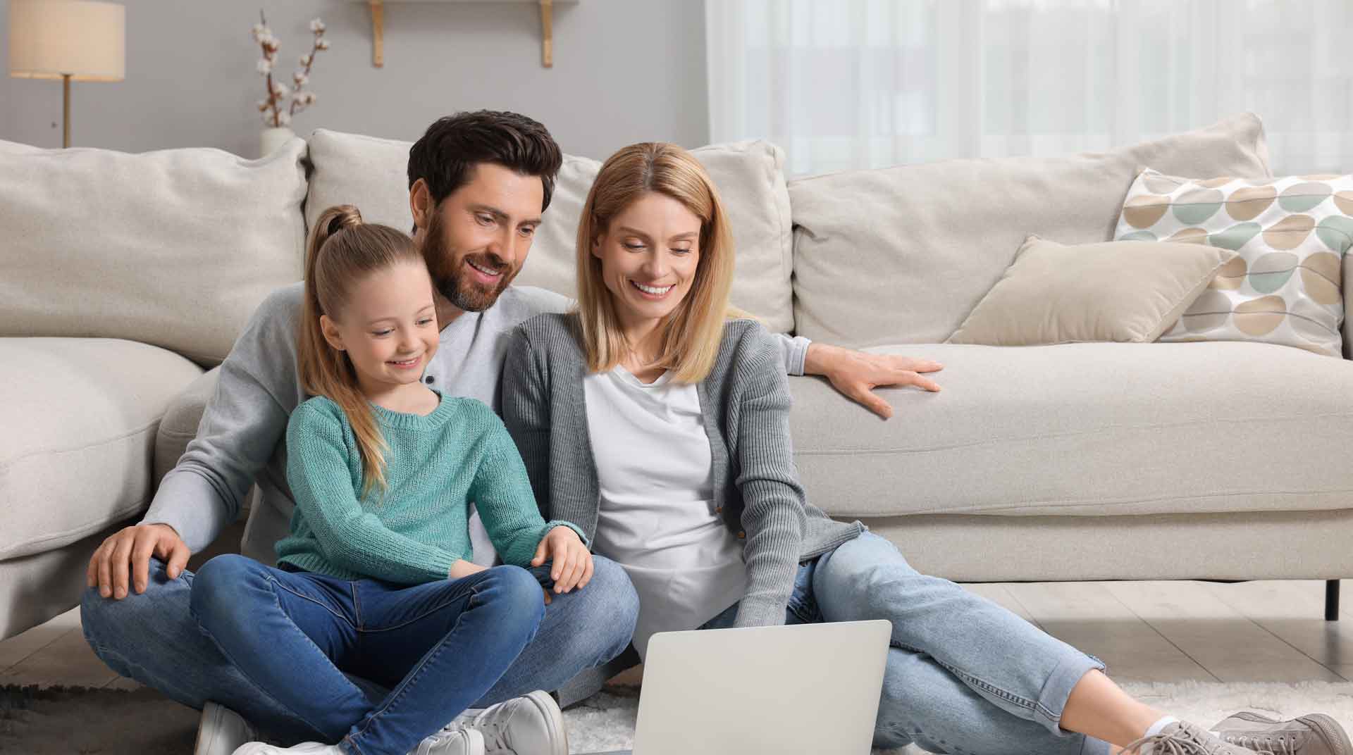 Mother and father sitting on their livingroom floor with their daughter on their lap while looking at a laptop