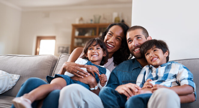 A happy family of four sits on a couch, smiling warmly. The parents, nestled in their cozy living room with an Empire Access Residential connection, hold their two young children. Behind them, a bookshelf completes the inviting scene.
