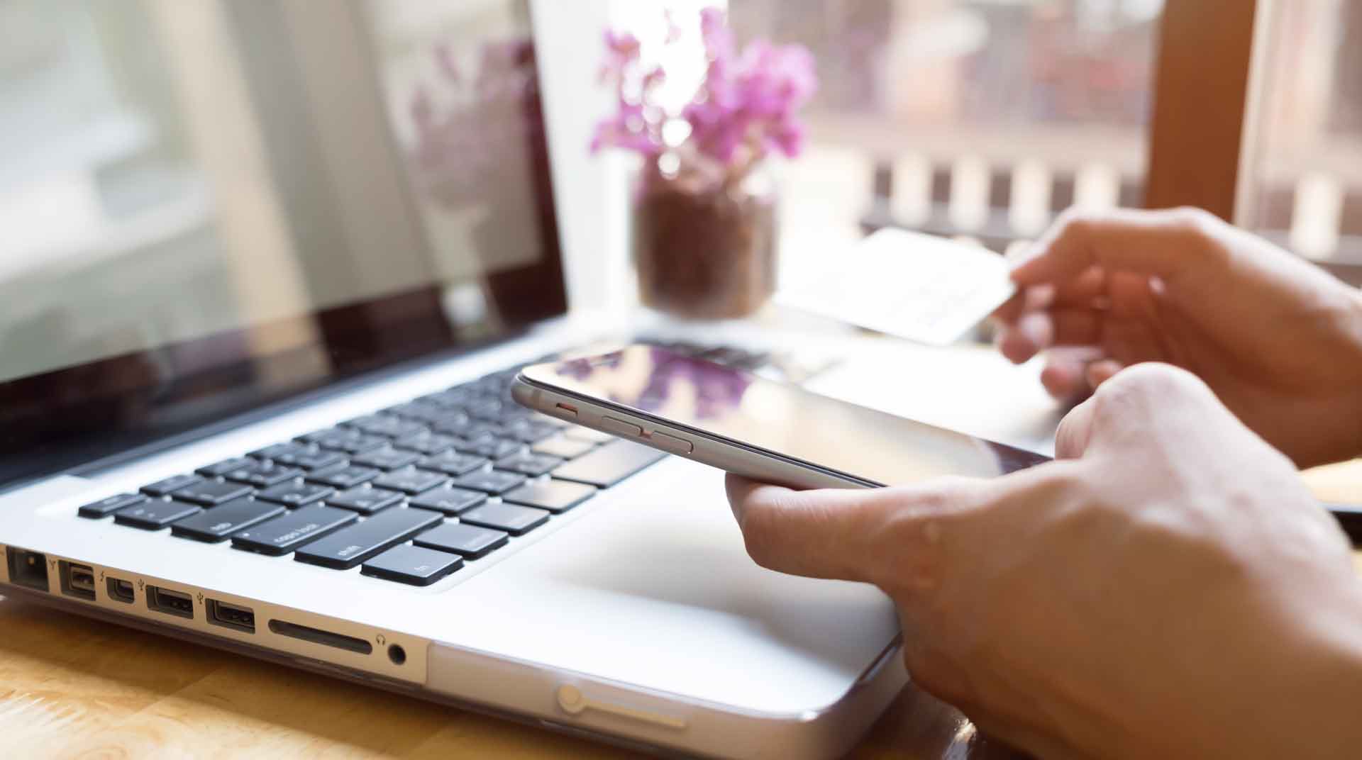 Close up of a woman holding her phone while sitting at a table with her laptop