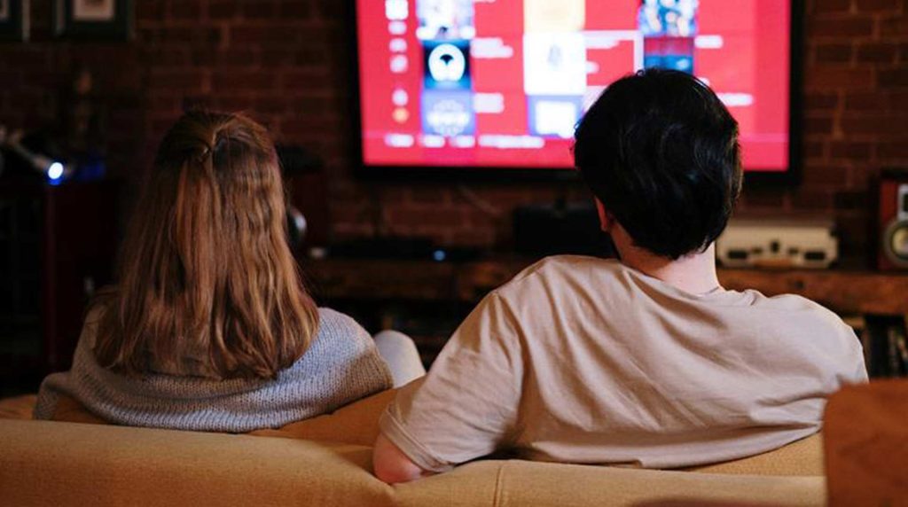 a man and woman are sitting on the couch watching tv