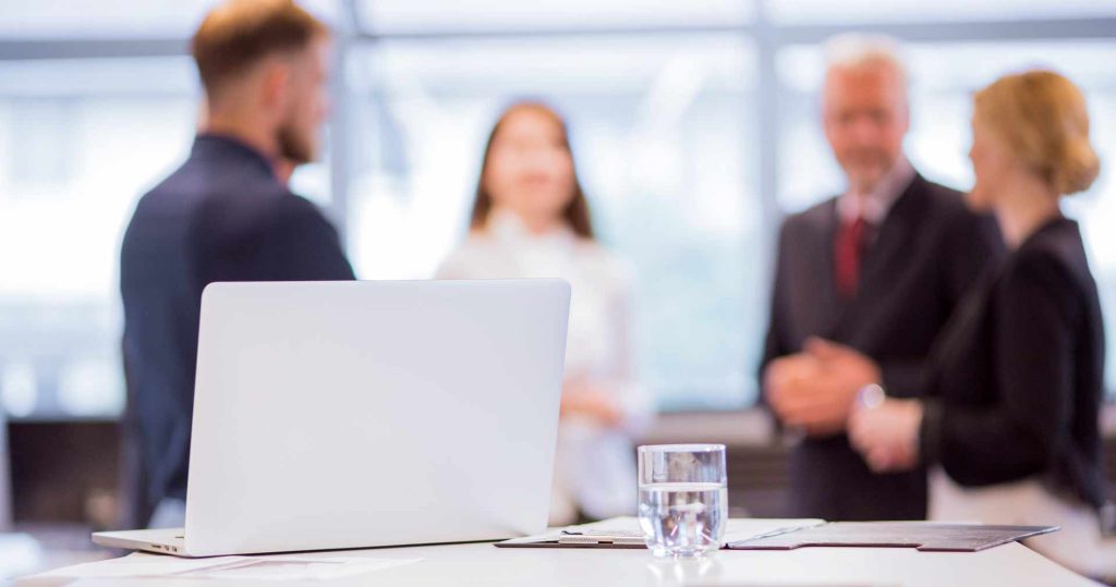 a gathering of business people talking with a laptop on the conference room table as the focal point