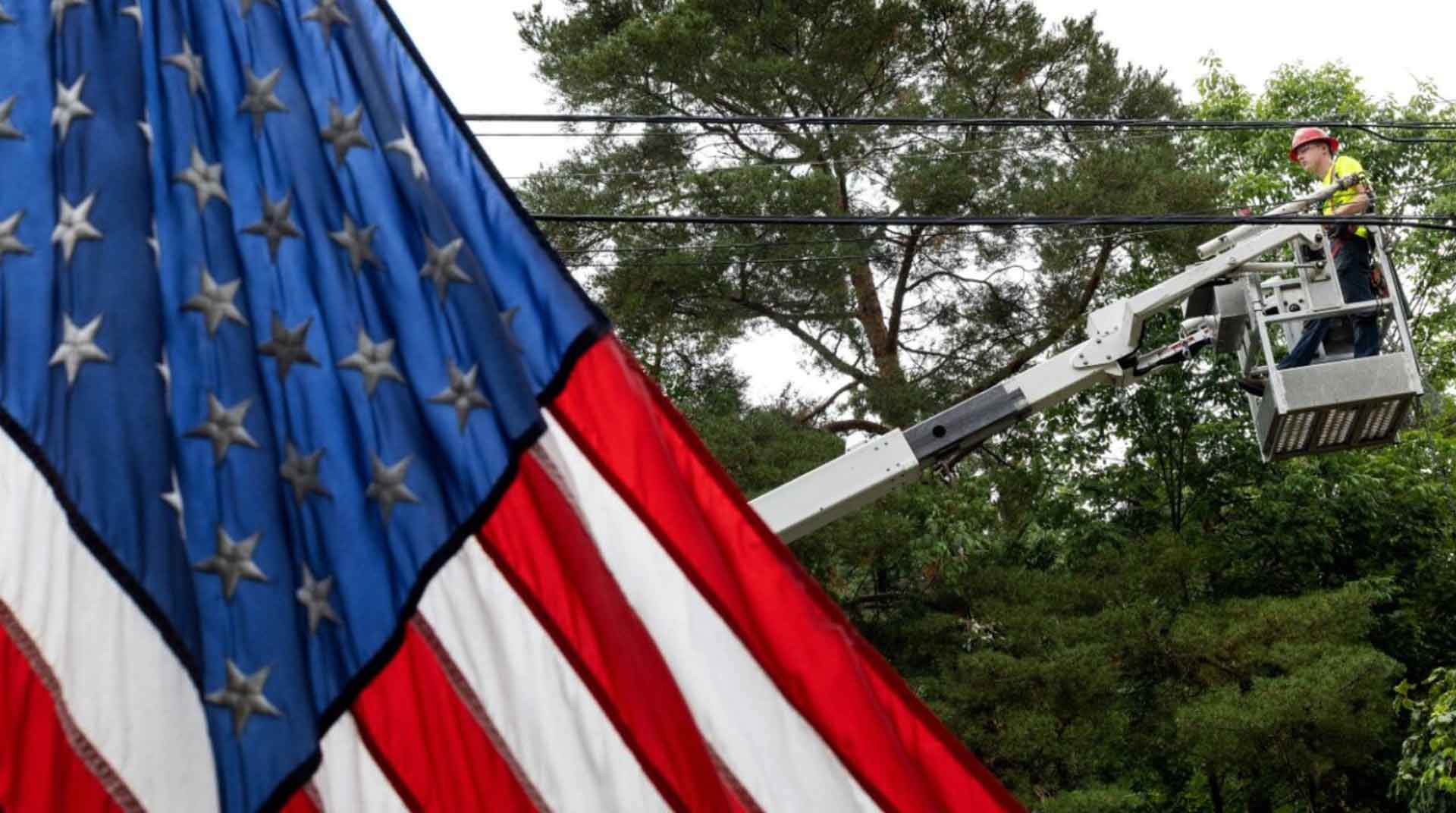 Closeup of the USA flag in the foreground with an Empire Fiber Internet employee in a bucket lift installing local fiber internet