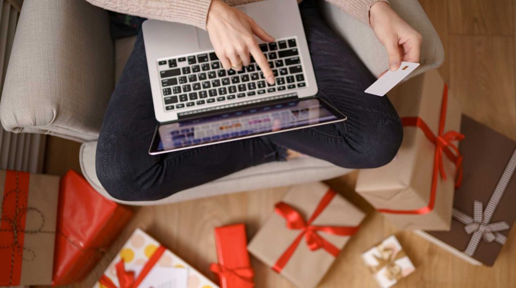 Closeup of person sitting on the floor surrounded by gifts while shopping online with their laptop using fiber internet