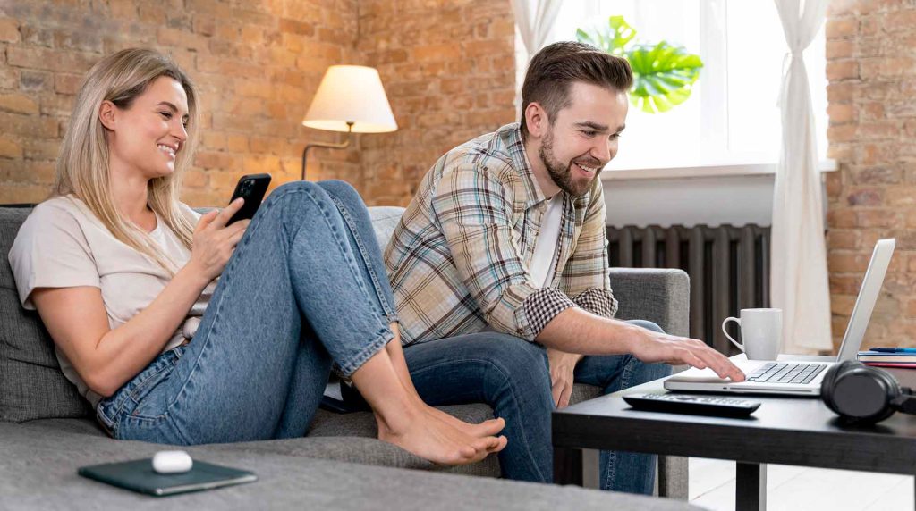 a couple sitting in their living room using whole home wi-fi on their phone and laptop