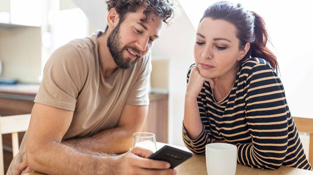 Man showing the Empire Fiber Internet Rewards Program on his phone to a woman sitting at a table with him